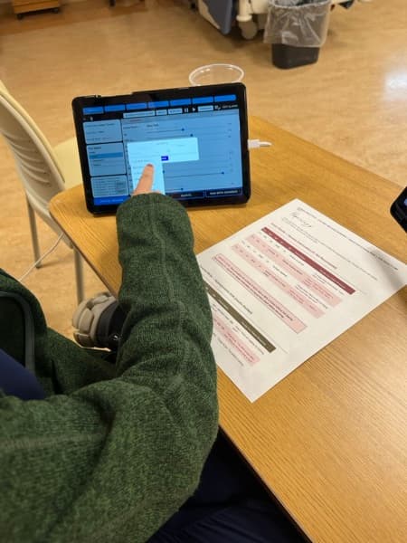 A student works a SimVS scenario on a tablet at the bedside table