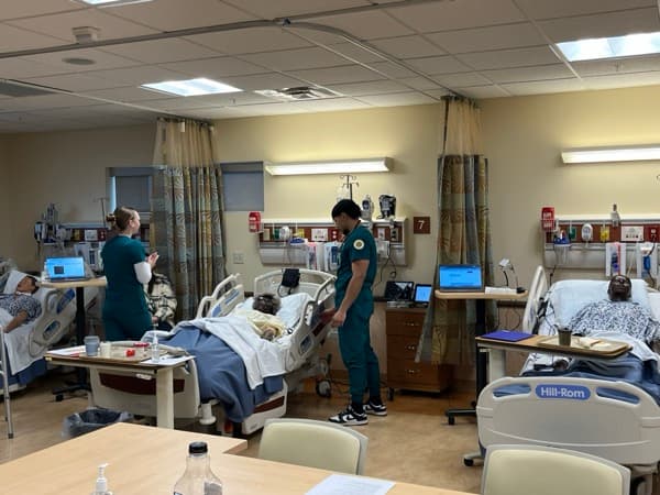Students working a multi-bed simulation lab with SimVS tablets at each bedside